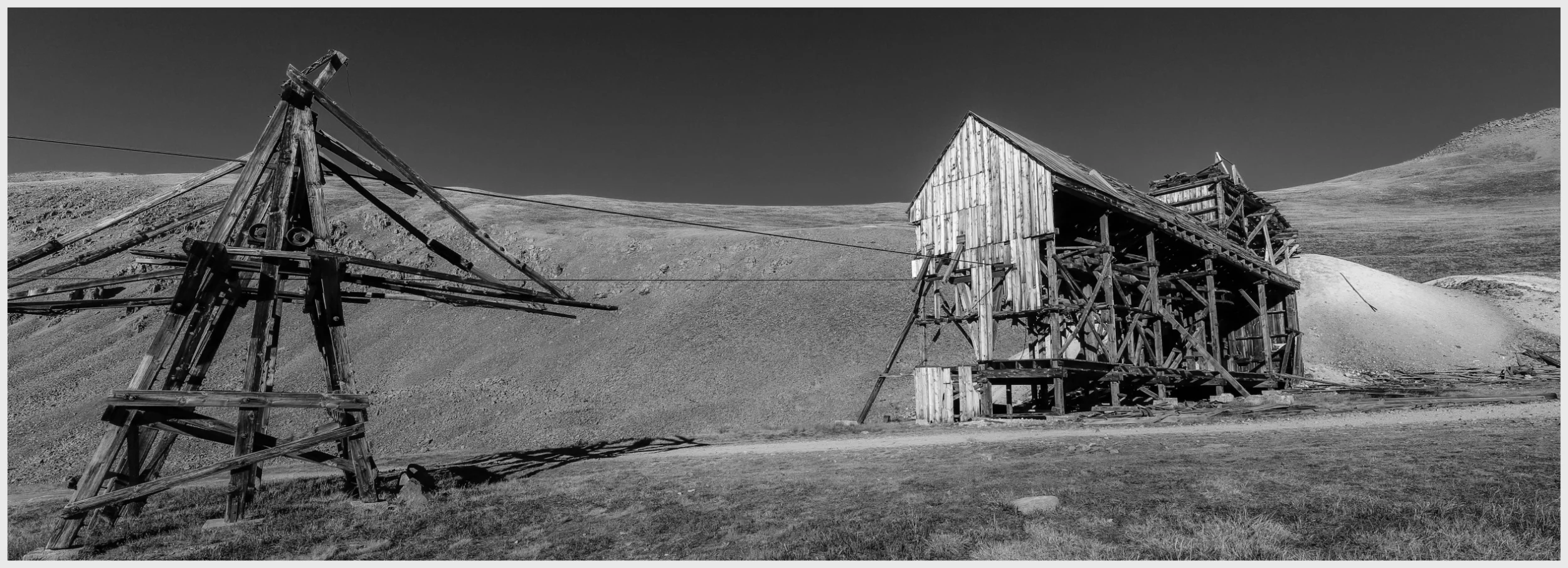 Near Silverton, Colorado, this photograph captures a 19th-century headframe and cable tower, relics from the silver rush era, starkly silhouetted against the landscape. These structures, weathered by decades, symbolize the spirit and endurance of miners who once delved deep into the earth in search of silver. Adjacent to the headframe, a mound of tailings serves as a tangible reminder of the laborious efforts to extract ore. The distinct crunch of these tailings underfoot as one walks among them echoes the hard work that characterized this historic period. The treeless expanse and biting cold of the high altitude highlight the miners' remarkable resilience in this harsh, stark environment, inviting reflection on the lasting impact of human ambition on the wild.